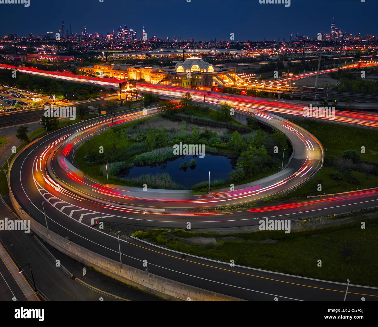 Secaucus Junction Station And NYC - Aerial long exposure view to the New Jersey Turnpike's very long ramp, the illuminated train station along  with a Stock Photo