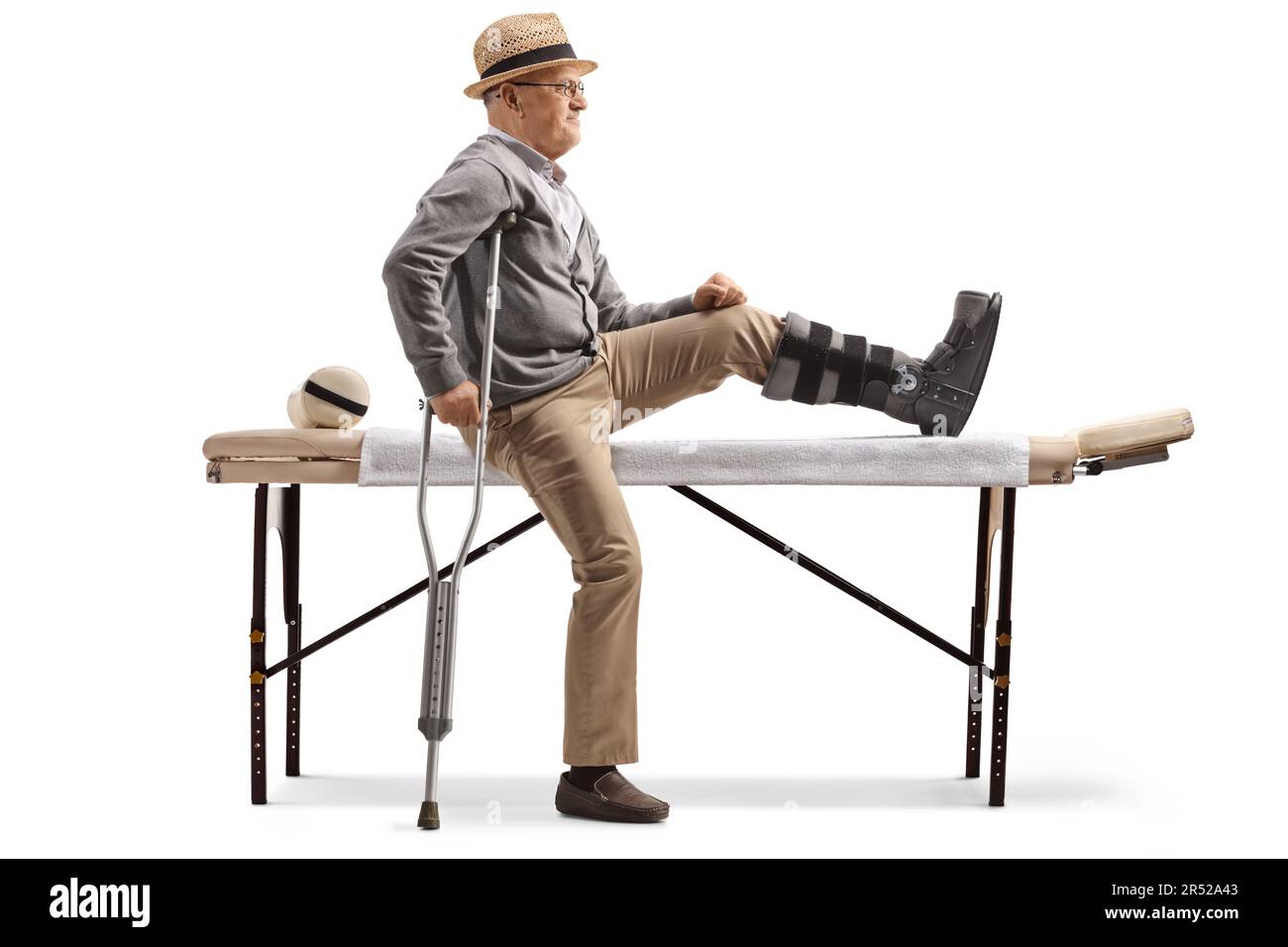 Elderly male patient sitting on a physical therapy bed with a brace on his leg isolated on white background Stock Photo