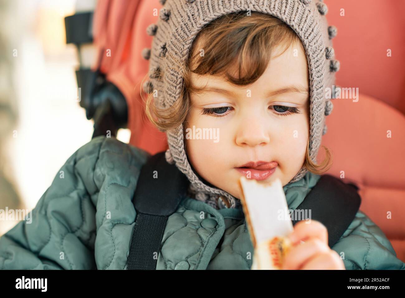 Happy toddler kid eating fruit bar, healthy snack, sitting in stroller