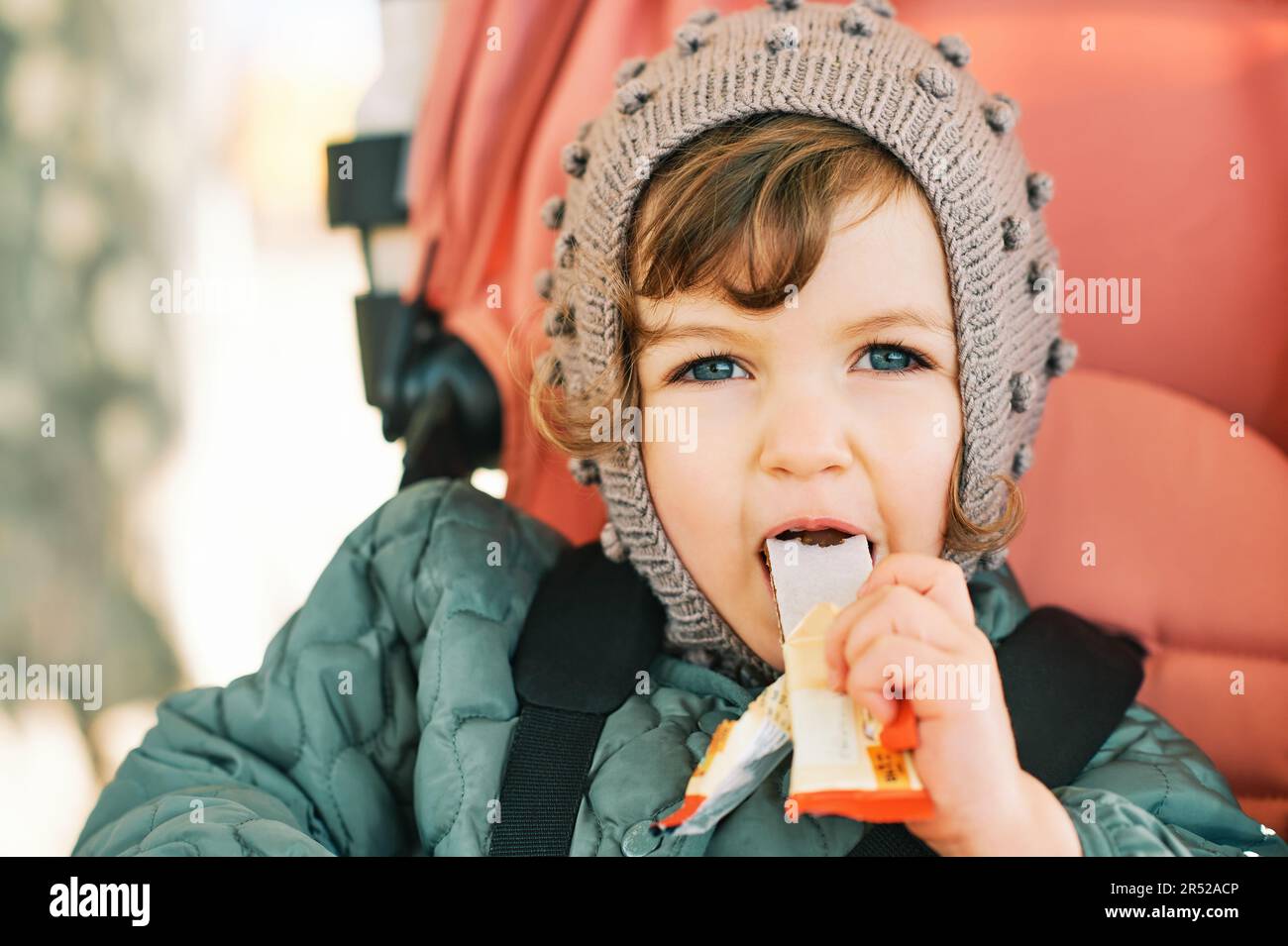 Happy toddler kid eating fruit bar, healthy snack, sitting in stroller