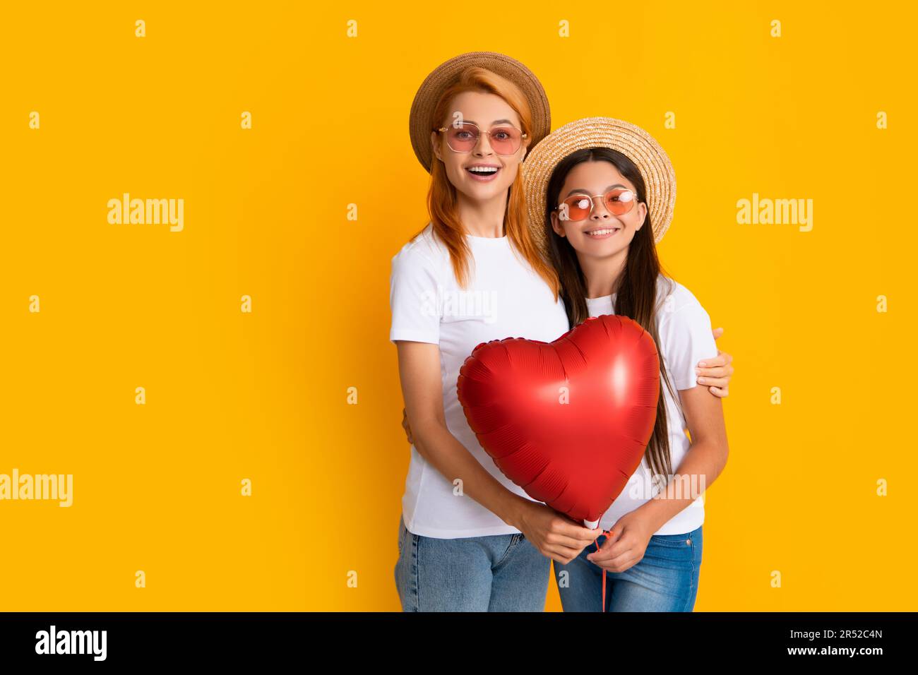 Valentines day. Smiling mother and daughter holding love heart balloon on yellow background. Happy Valentines day to my mom. Love summer. Stock Photo