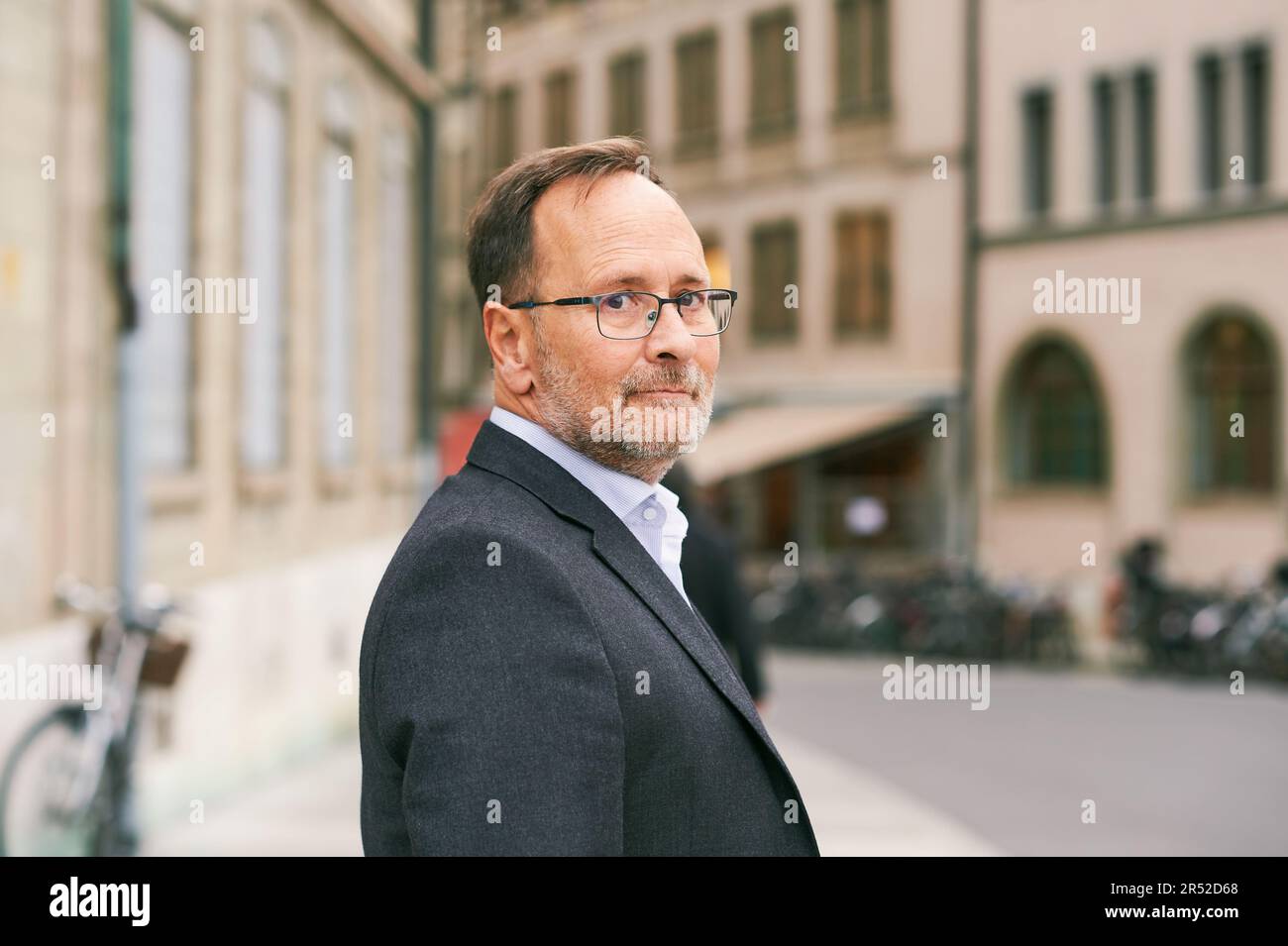 Outdoor portrait of middle age man looking back over the shoulder, wearing glasses and grey suit Stock Photo