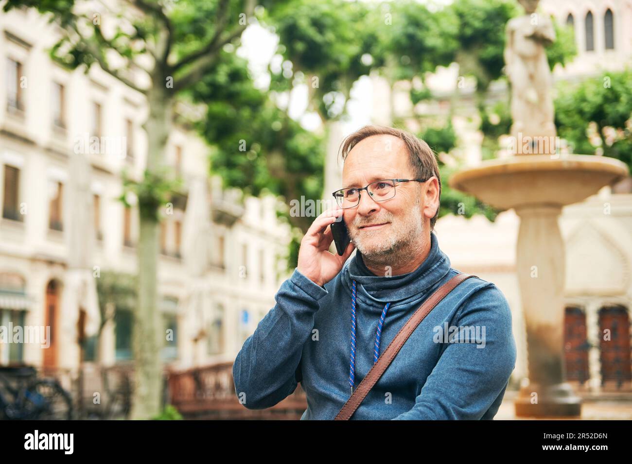 Outdoor portrait of middle age man talking on the phone, wearing glasses and blue sweatshirt, holding smartphone next to ear Stock Photo