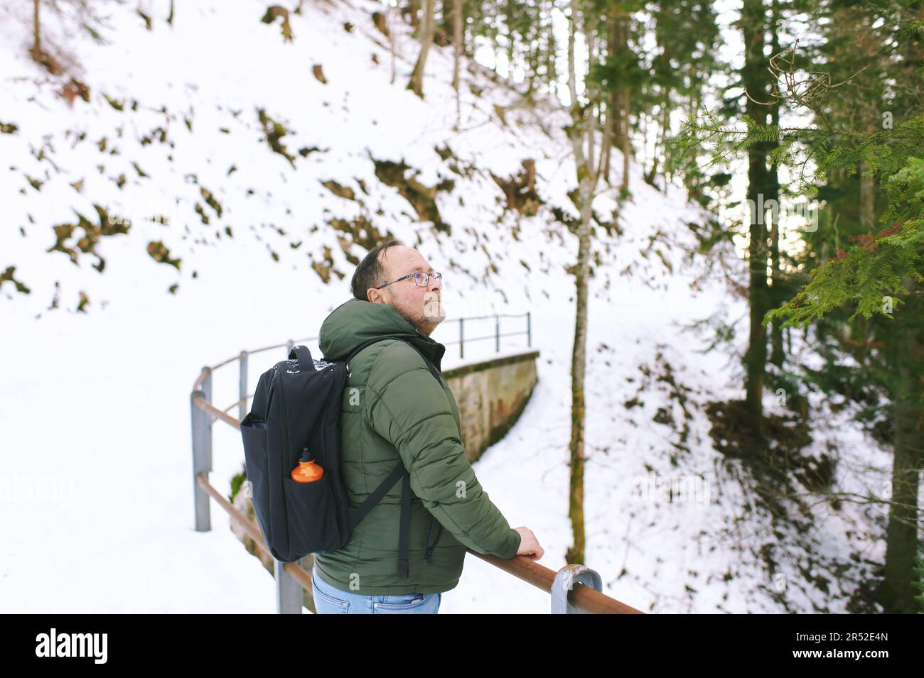 Outdoor portrait of middle age 55 - 60 year old man hiking in winter forest, wearing warm jacket and black backpack Stock Photo