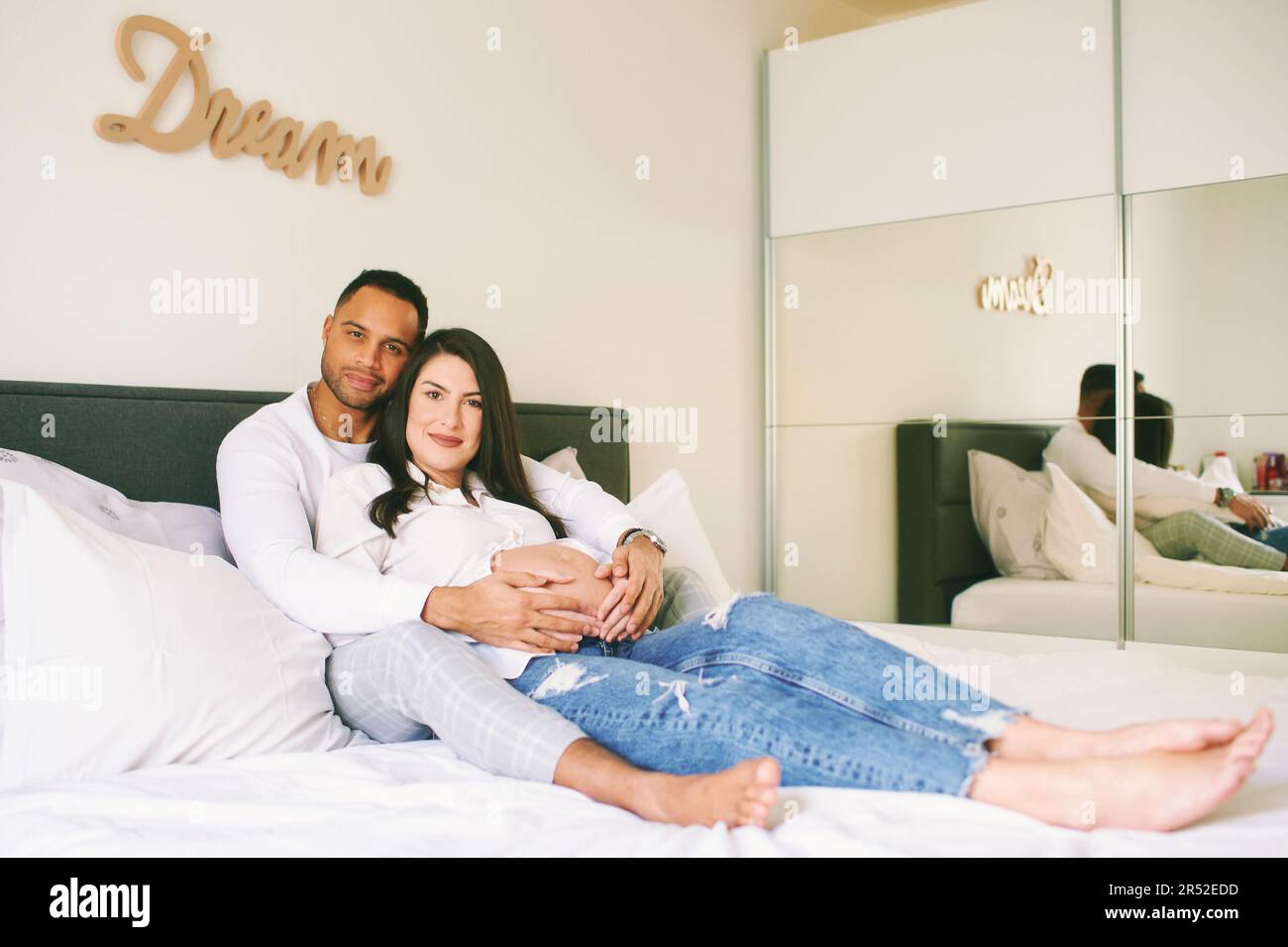 Indoor portrait of happy young family, pregnant woman with her loving husband relaxing on bed Stock Photo