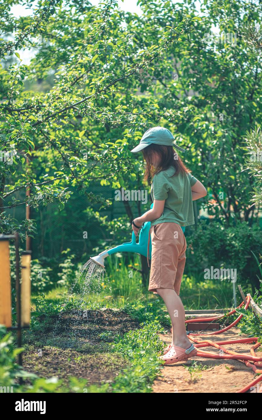 Little girl watering blooming tree with watering pot in the garden. Kid