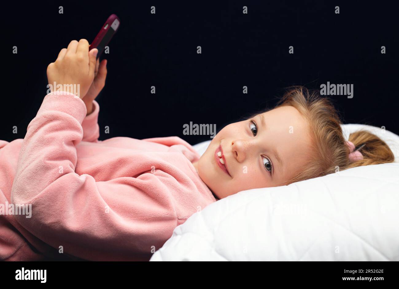 kid girl lying in bed playing a smartphone Stock Photo