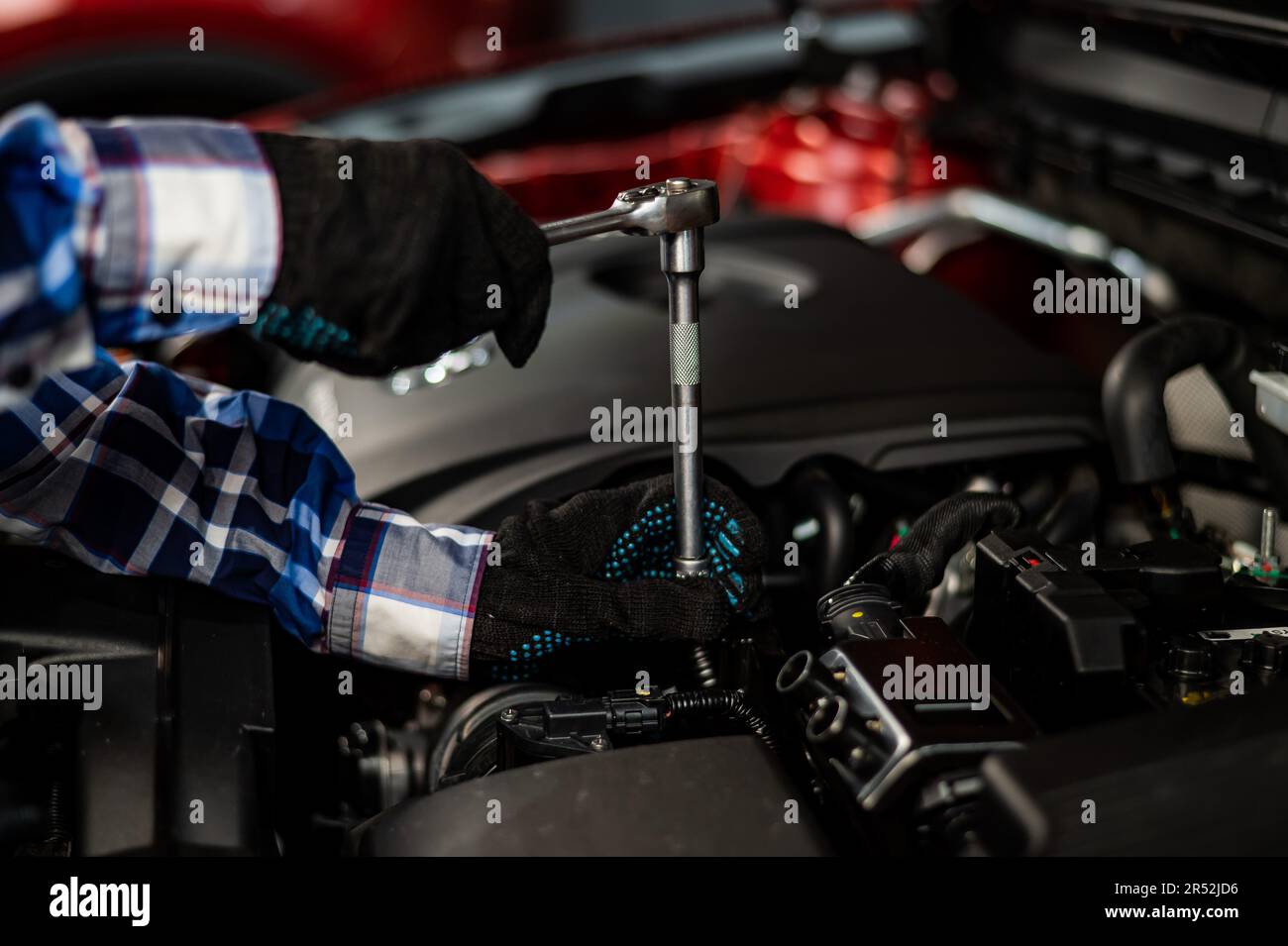 Female auto mechanic unscrewing a nut to replace a car spark plug Stock