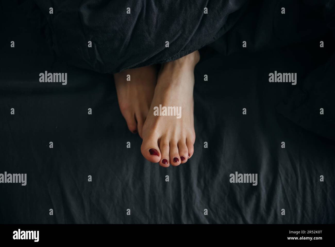 Women's legs with a pedicure stick out from under the blanket in bed
