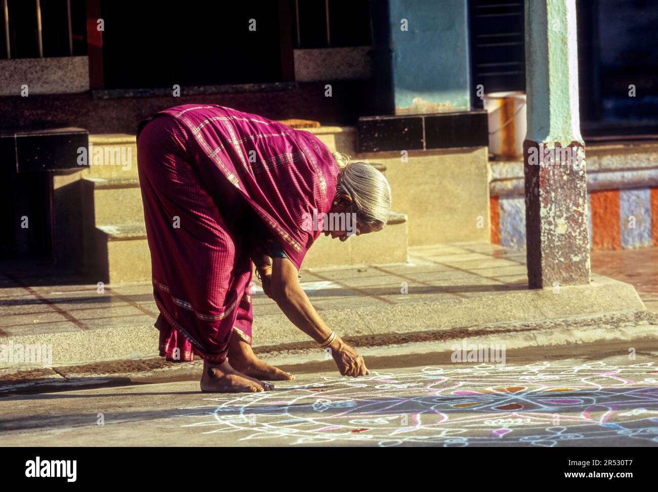 A Brahmin woman drawing a kolam in front of her Agraharam house wearing