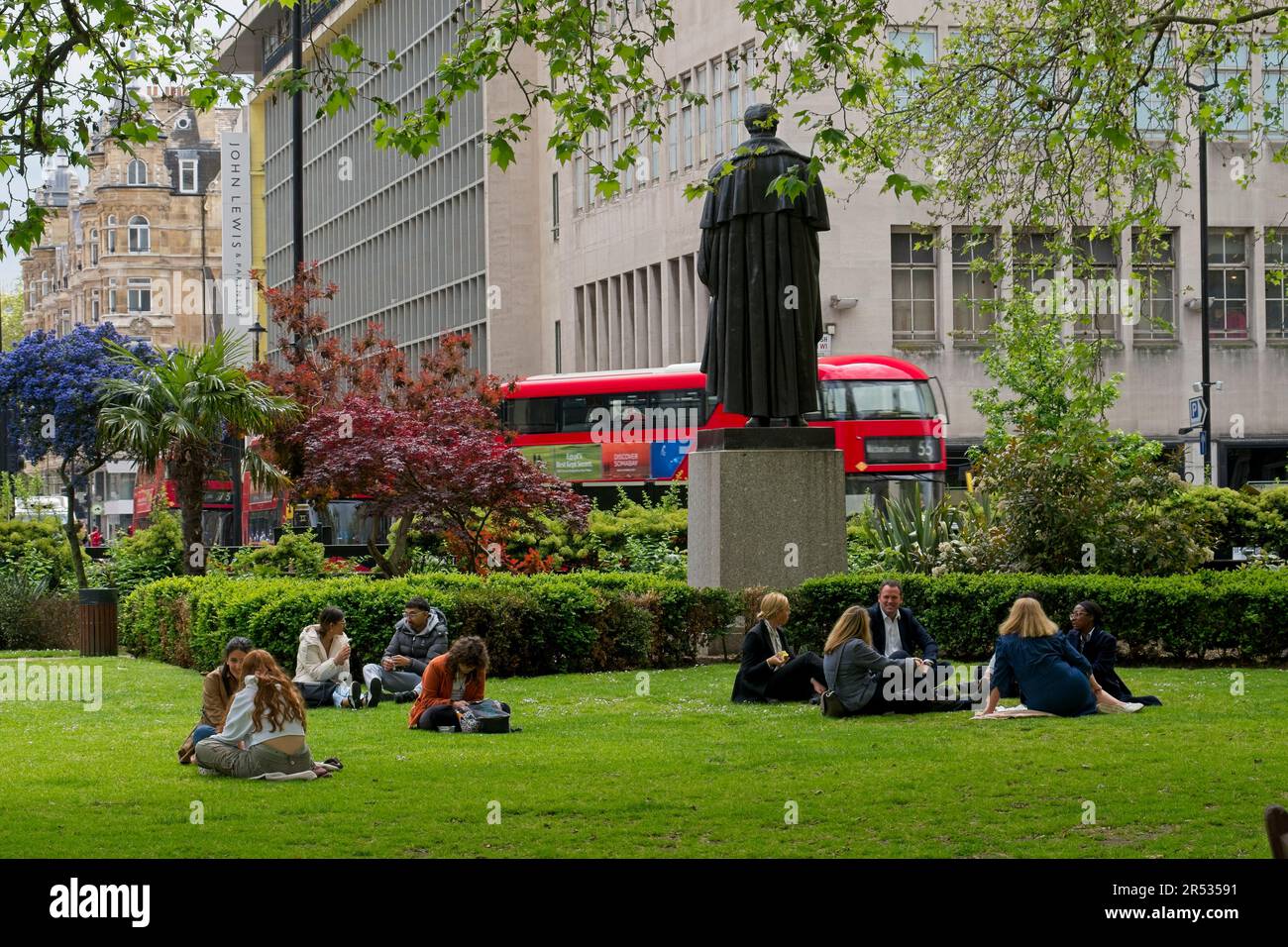 Cavendish Square London W1 England UK Sunshine with people sitting on grass below statue of Lord George Bentinck. Buildings and traffic behind. Stock Photo