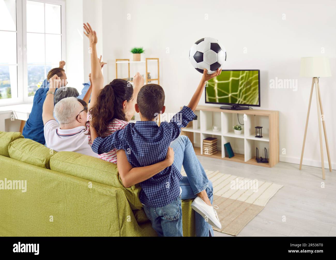 Excited happy big family cheering watching American football championship game on TV. Stock Photo