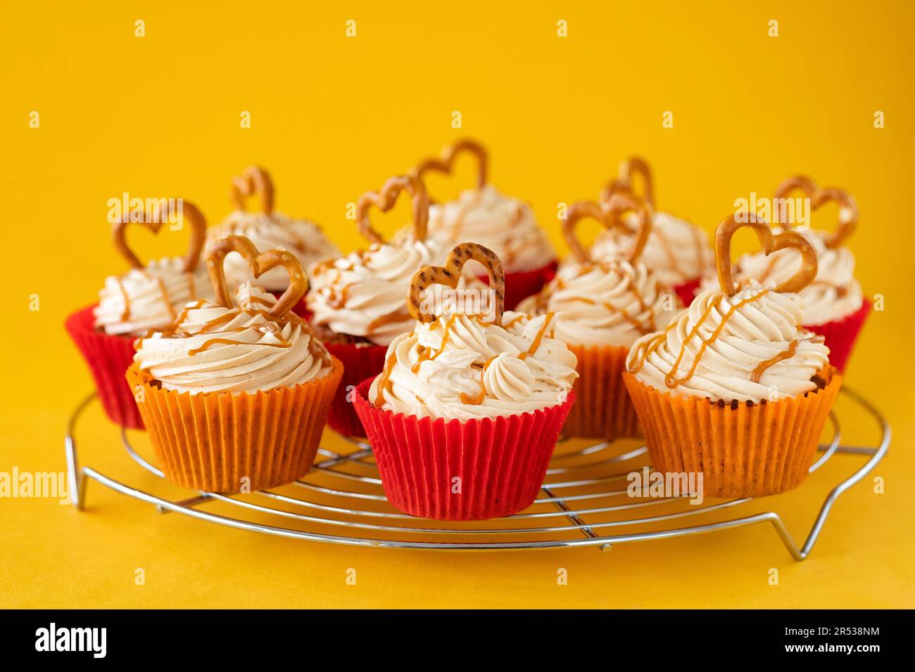 A batch of home made caramel pretzel cupcakes. The cakes are shown on a cooling rack and have a buttercream topping decorated with a pretzel Stock Photo