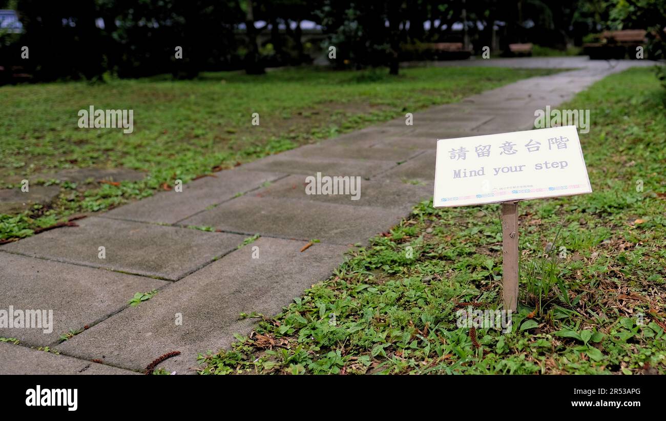 Bilingual faded Mind Your Step sign warning visitors at Chiang Kai-Shek Memorial Hall to walk with care along the paved path; Taipei, Taiwan. Stock Photo