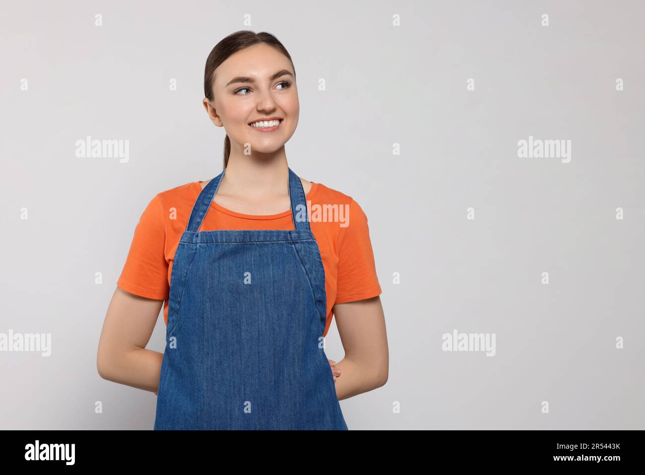Beautiful young woman in clean denim apron on light grey background ...