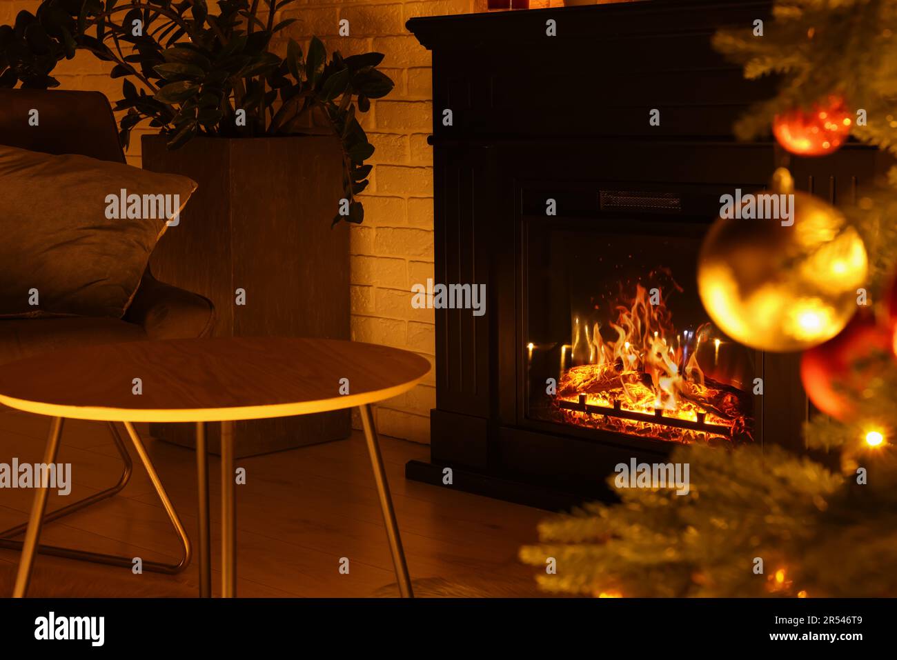 Christmas tree with baubles near cosy fireplace indoors Stock Photo