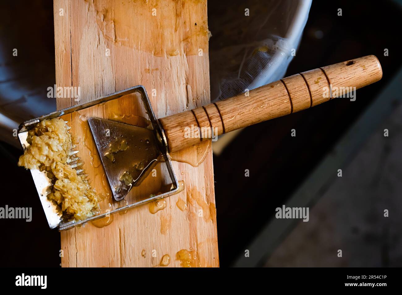 A honey uncapping tool with beeswax on it sitting on a wood board Stock Photo