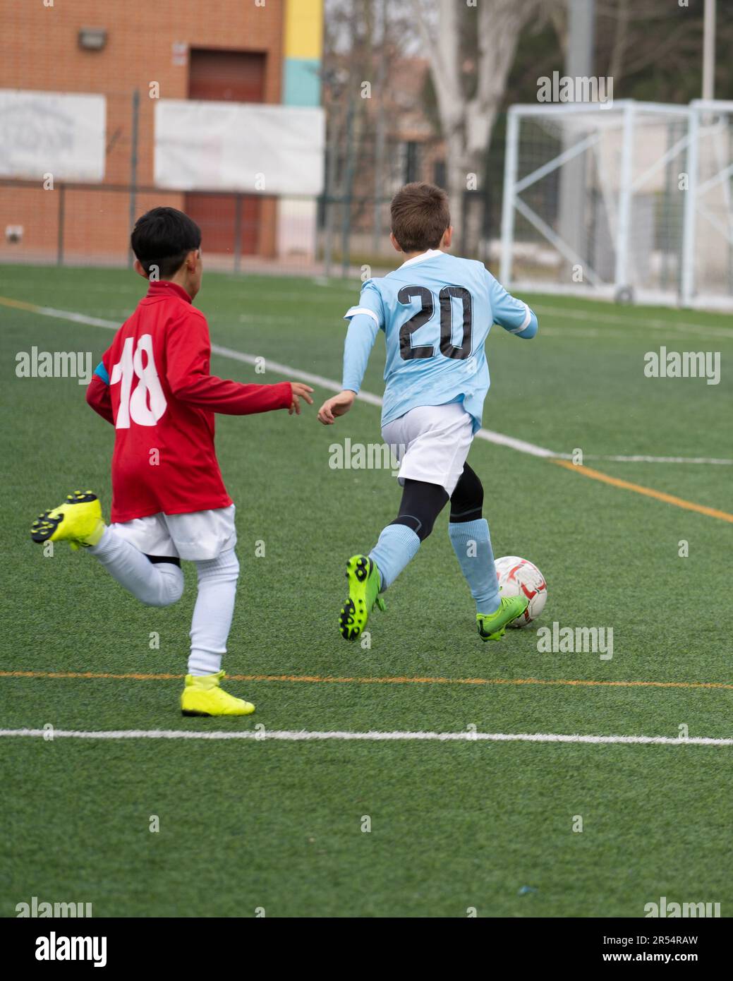 Two young soccer players kicking soccer ball on grass pitch. Youth sports competition between two school sports teams.  Stock Photo