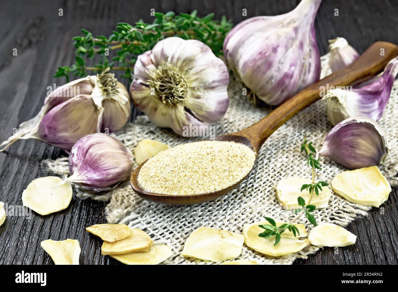 Ground garlic in a spoon on burlap, dried and fresh garlic, bunch of thyme on black wooden board background Stock Photo