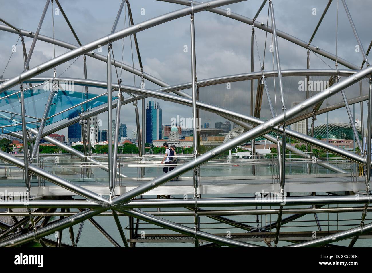 A tourist couple crossing over Marina Bay, Singapore, via the iconic, futuristic Helix Bridge, its design inspired by the shape of human DNA Stock Photo
