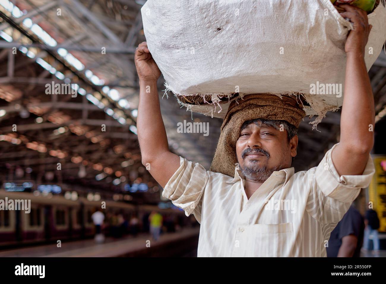 A porter at Chhatrapati Shivaji Maharaj Terminus (CSMT), Mumbai, India, carrying a large basket on his head to forward to a train's goods compartment Stock Photo