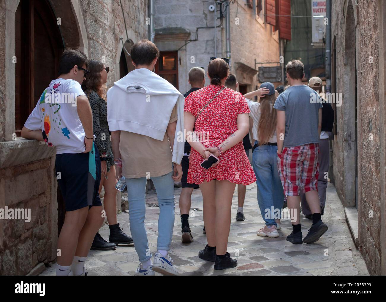 Kotor, Montenegro, Apr 12, 2023: View from behind of a young woman with tattooed hands in a group of tourists walking down the street Stock Photo