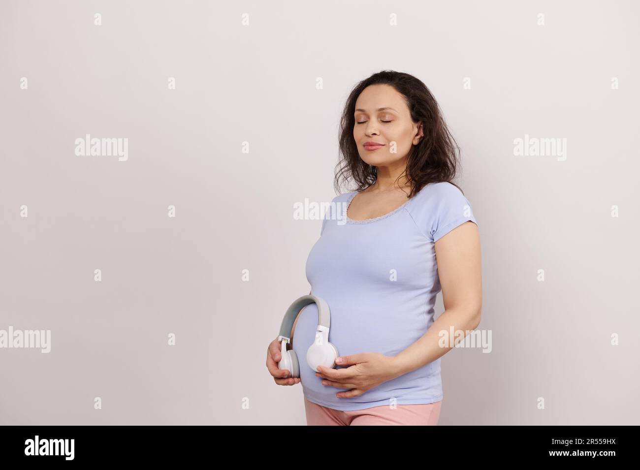 Pregnant woman putting wireless headphones over her belly, turning on