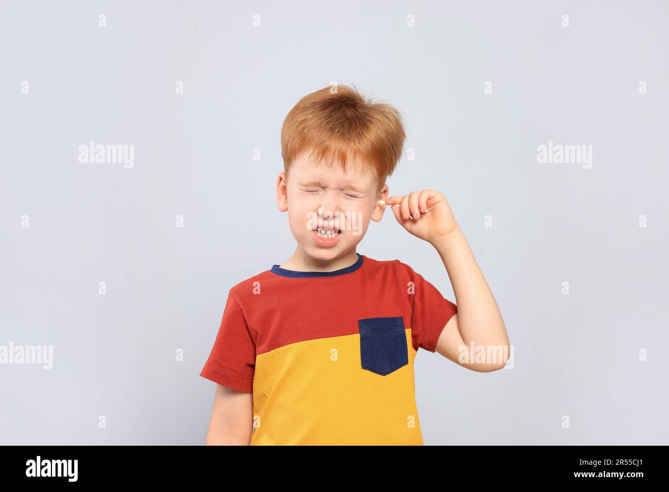 Little boy cleaning ear with cotton swab on light grey background Stock