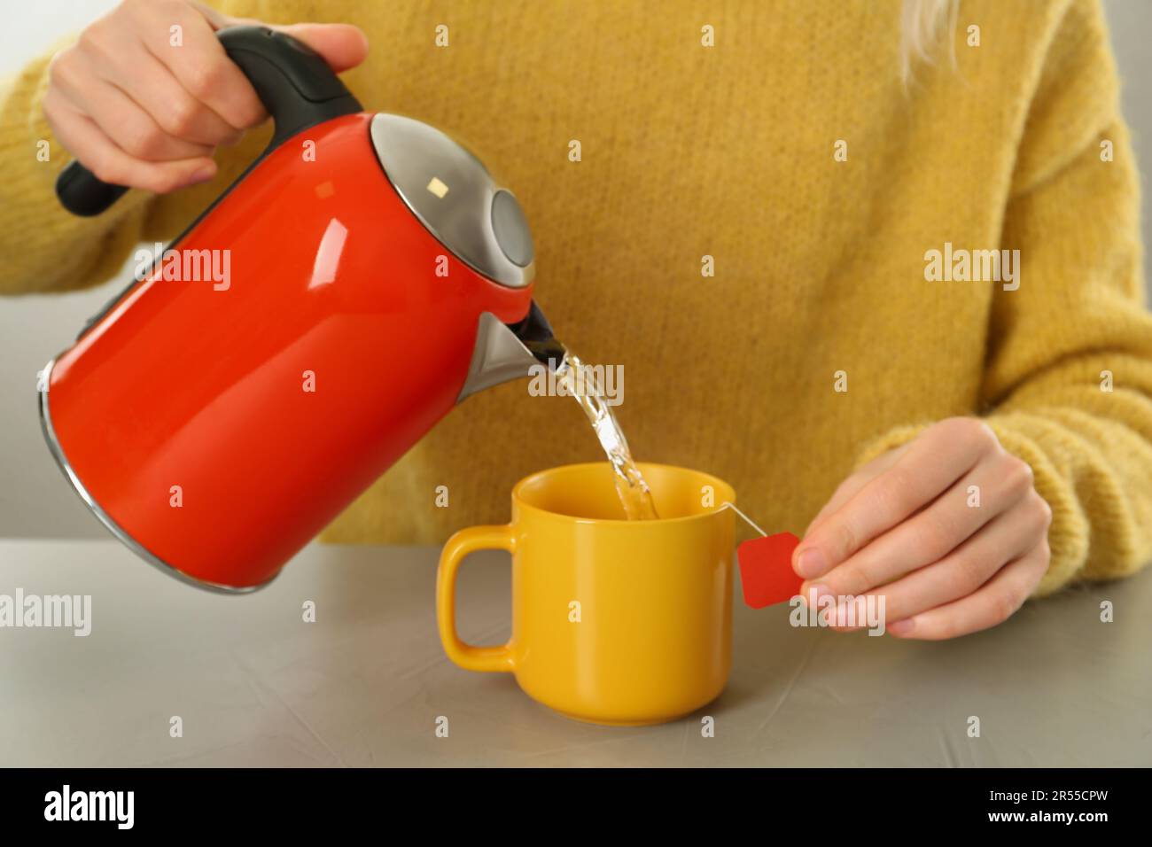 https://c8.alamy.com/comp/2R55CPW/woman-pouring-hot-water-into-cup-with-tea-bag-at-grey-table-closeup-2R55CPW.jpg