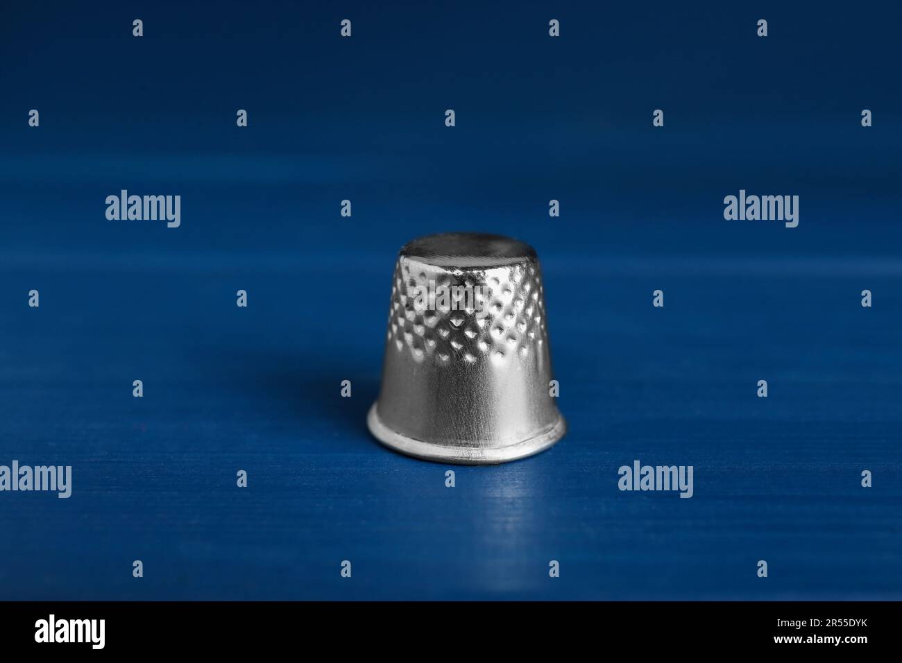 Silver thimble on blue wooden table. Sewing accessory Stock Photo