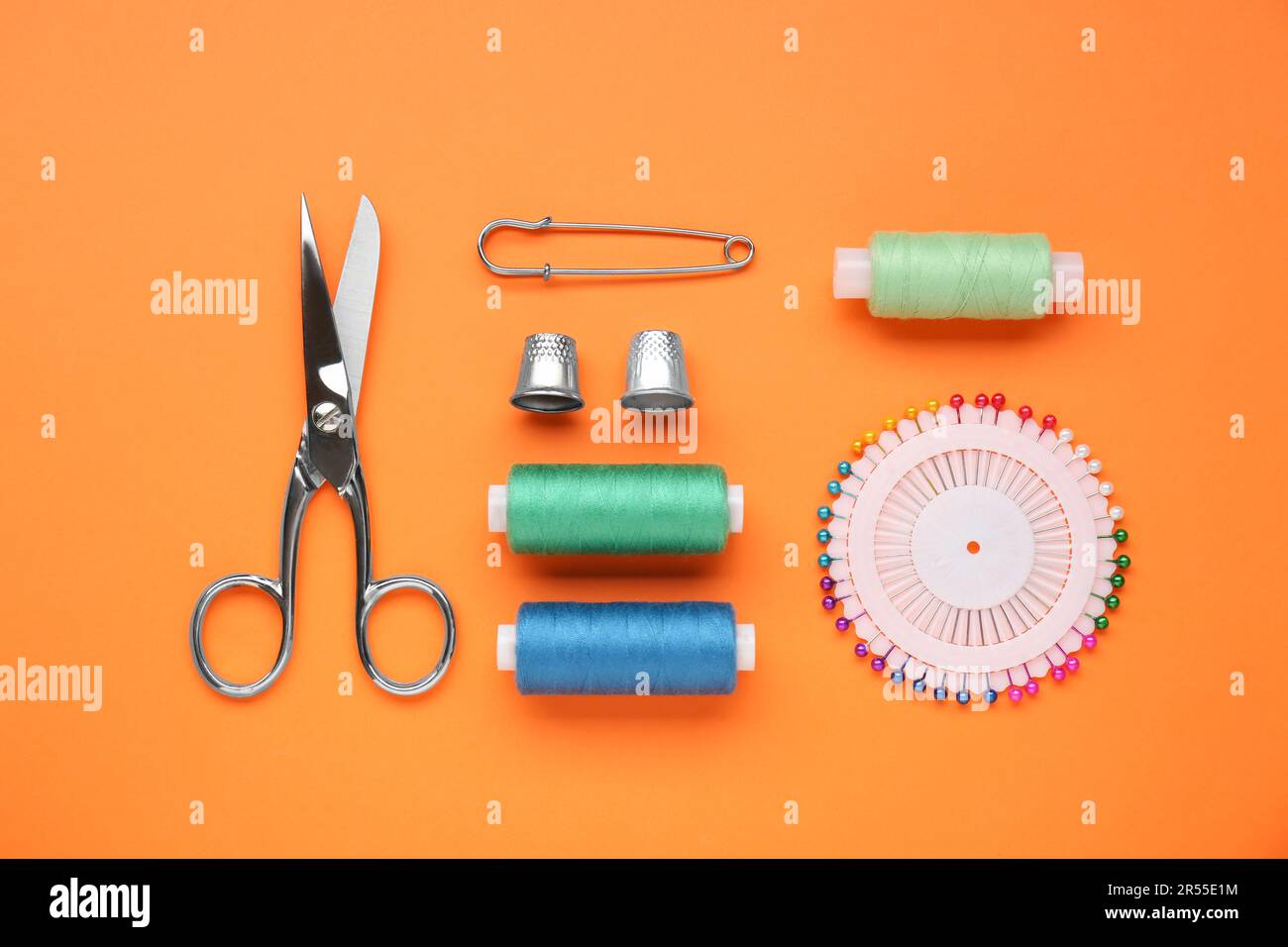 Flat lay composition with thimbles and different sewing tools on orange background Stock Photo