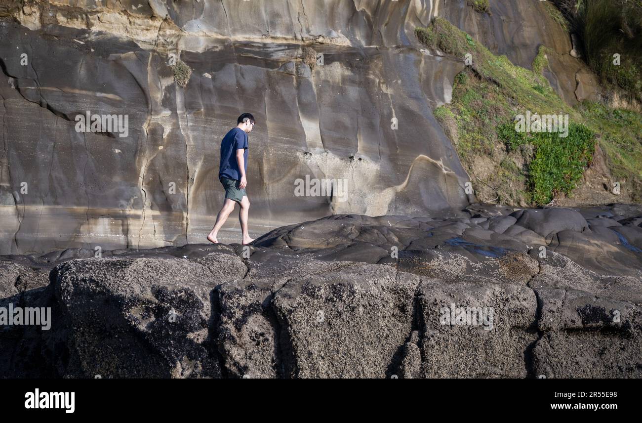 Man walking barefoot on rocks at Muriwai beach. Auckland. Stock Photo