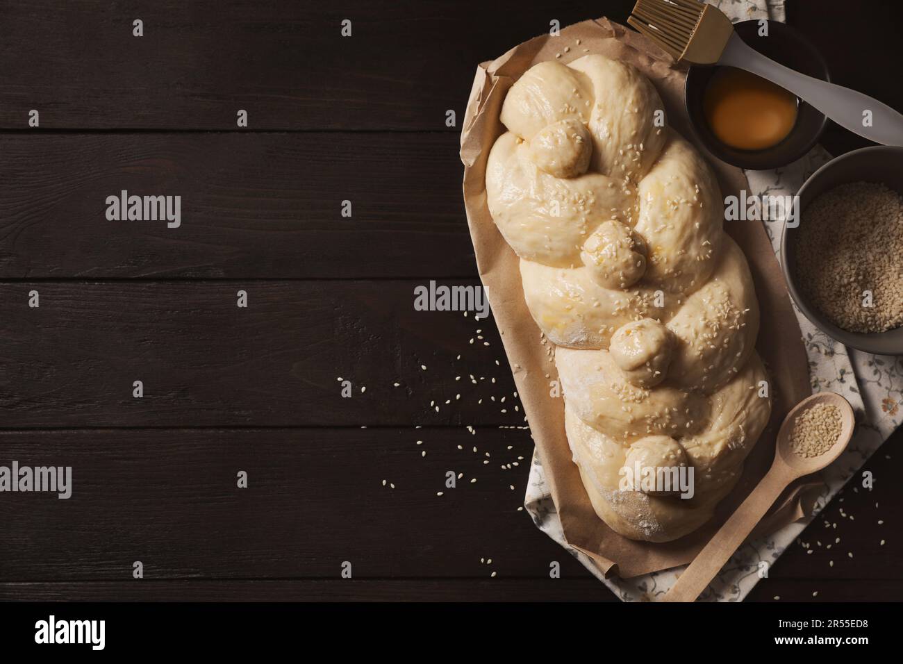 https://c8.alamy.com/comp/2R55ED8/raw-braided-bread-ingredients-and-pastry-brush-on-black-wooden-table-flat-lay-with-space-for-text-traditional-shabbat-challah-2R55ED8.jpg
