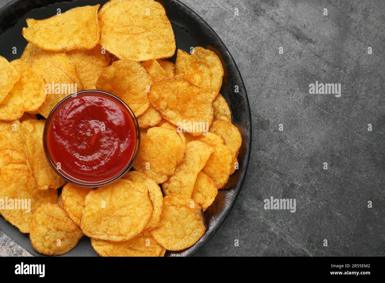 Delicious chips with ketchup on grey table, top view. Space for text