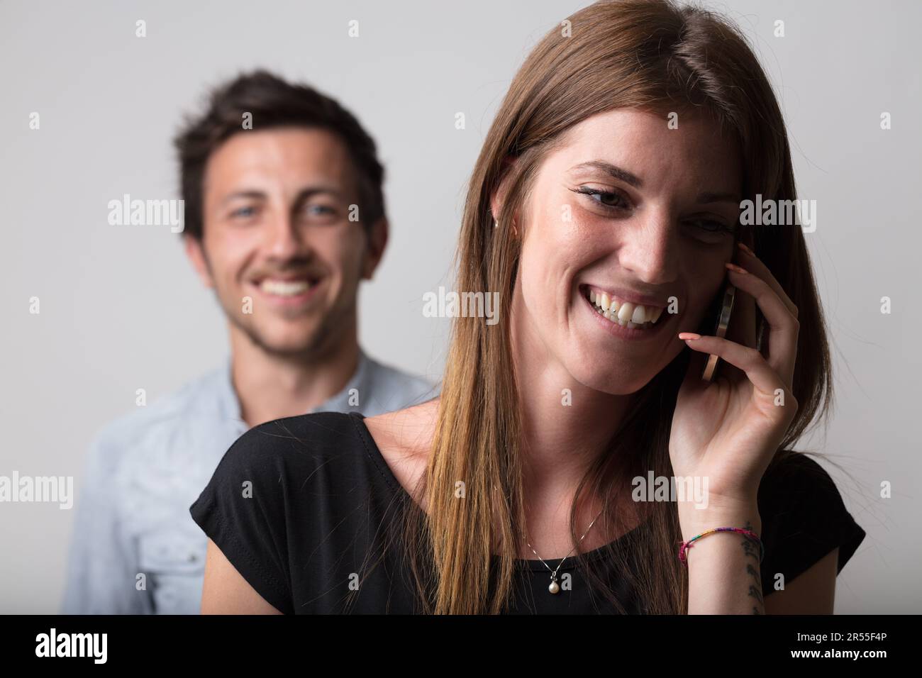 A woman on a phone call takes the foreground, with a blurred, suspicious young man in the backdrop. It insinuates betrayal, jealousy, love, stormy rel Stock Photo