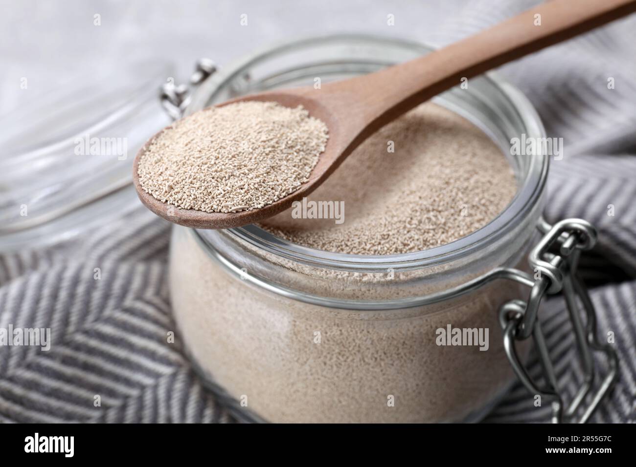 Glass jar and spoon with active dry yeast on light grey table, closeup