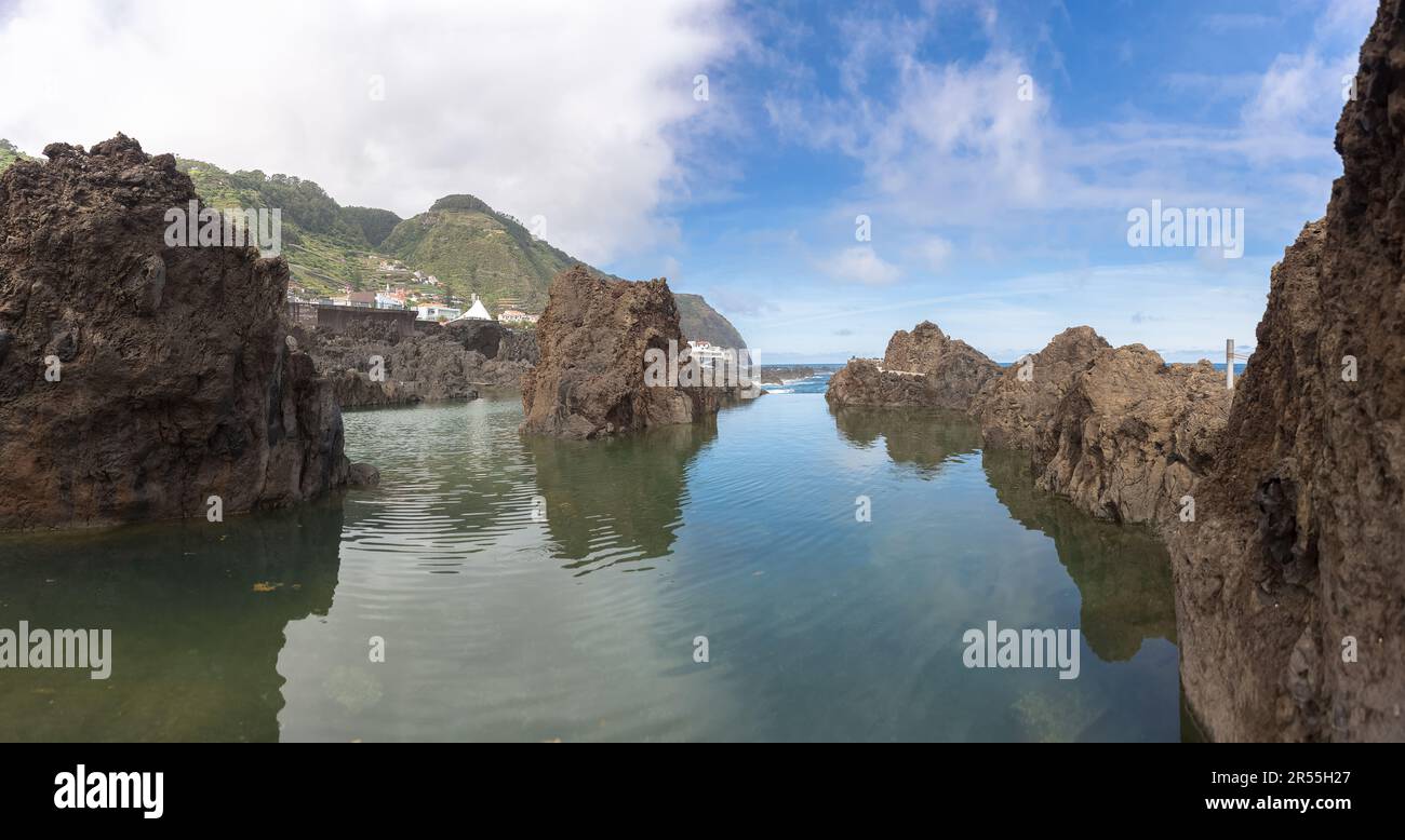 Madeira Island Portugal - 04 19 2023: Panoramic view of the natural pools on village of Porto Moniz, formed by volcanic rocks, village buildings in th Stock Photo
