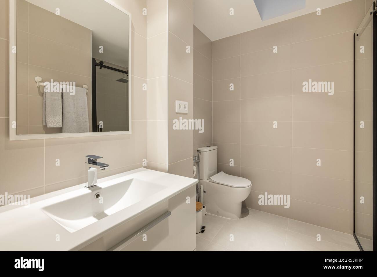 Stylish spacious bathroom with toilet, shower and sink with cabinet and mirror in beige tones in a new building. Concept of convenient and concise Stock Photo