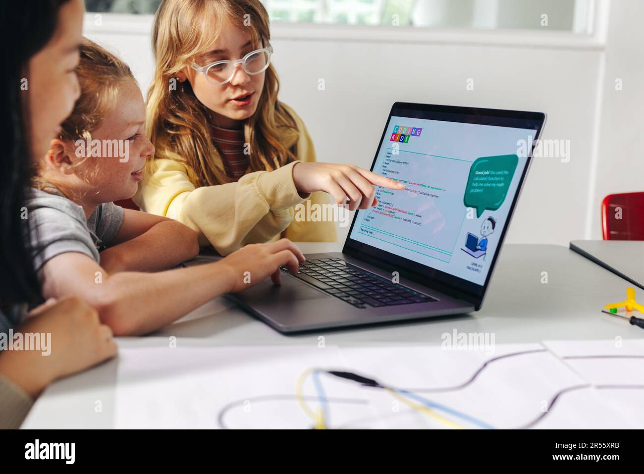 Smart young girl explaining robot programming to classmates in a computer science lesson. Boys and girls assist each other to develop skills in roboti Stock Photo