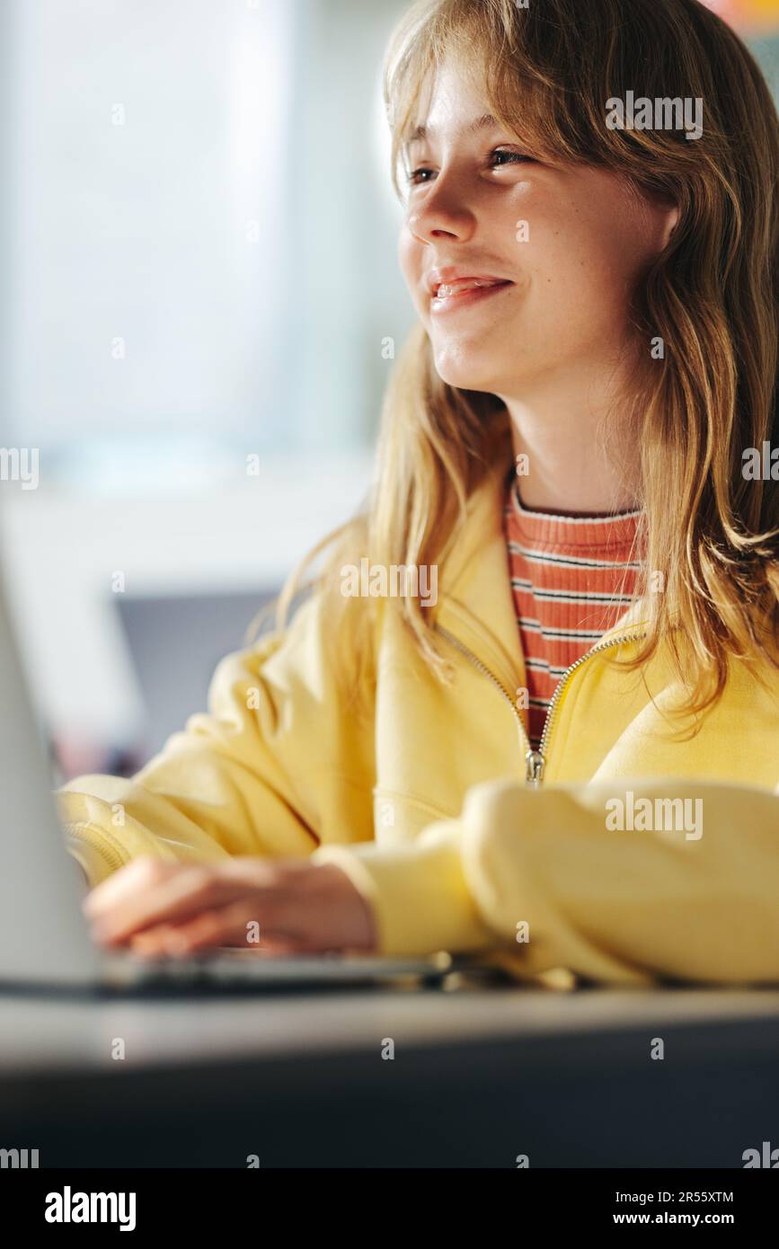 Happy young girl paying attention to a digital literacy lesson with a smile on her face. Sitting at her desk with a laptop, she is eager to learn and Stock Photo