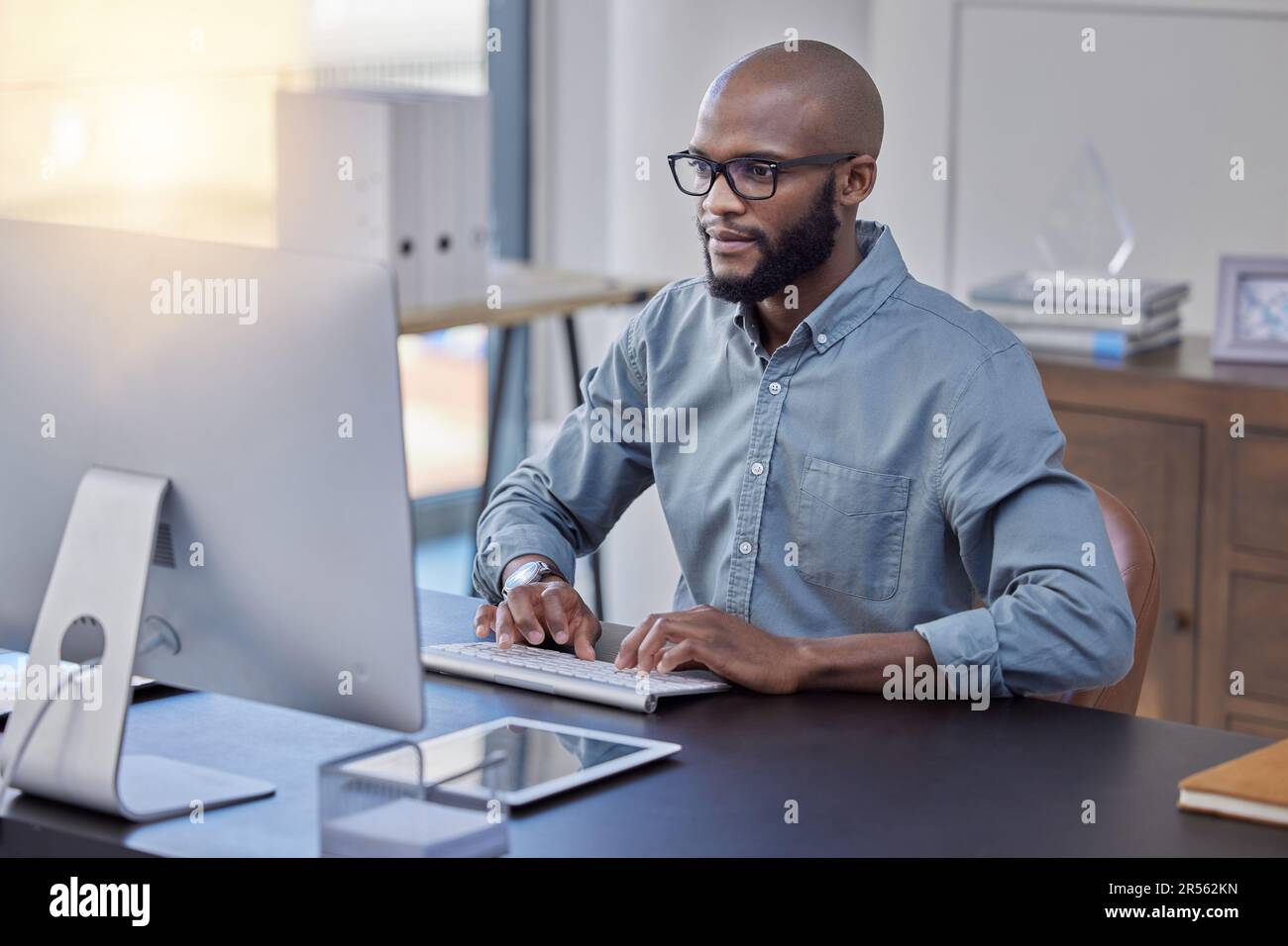 Programmer, computer and black man typing for software, coding or email in office. IT, desktop and African professional working on cyber security Stock Photo