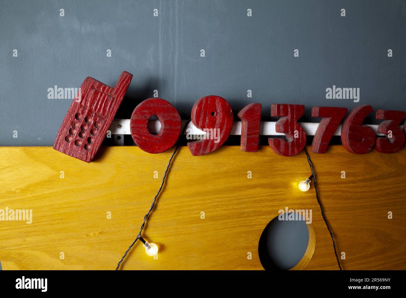 Red wooden sawn out digits of a mobile phone number as an advertisement of services. Rustic 3D handmade cellphone number on a store facade Stock Photo