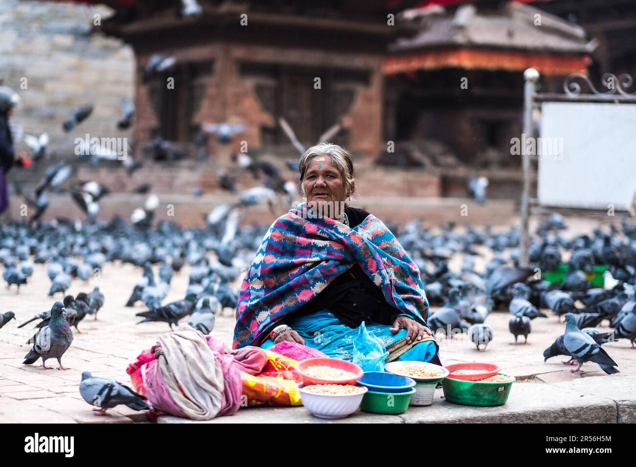 Kathmandu, Nepal - 06 October 2017: Old Nepalese woman in colorful traditional clothes selling corn seeds at the street market on Durbar square with pigeons all around, Kathmandu, Nepal Stock Photo