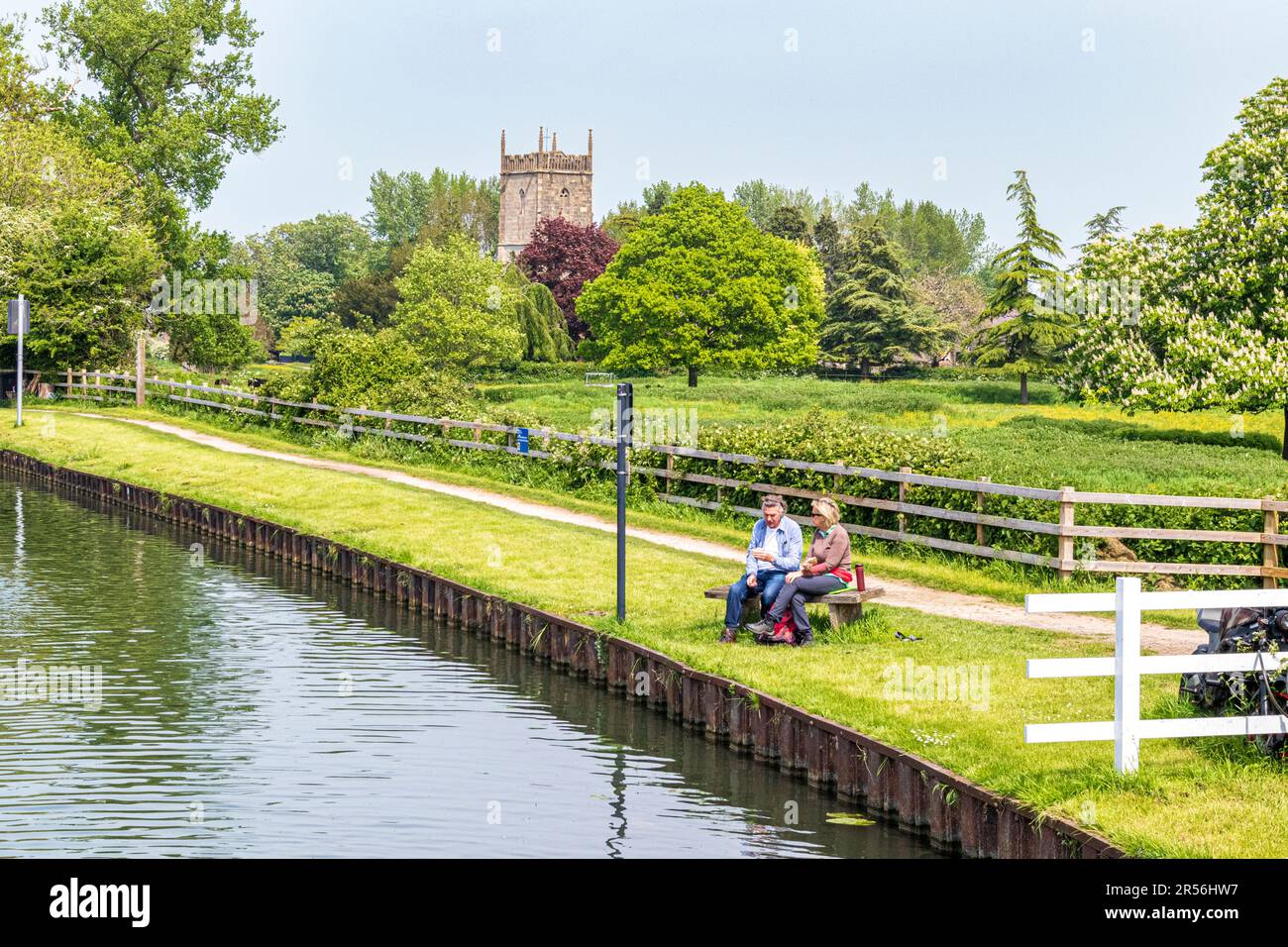 A couple picnicking beside the Gloucester and Sharpness Canal and St Marys church in the Severnside village of Frampton on Severn, Gloucestershire UK Stock Photo