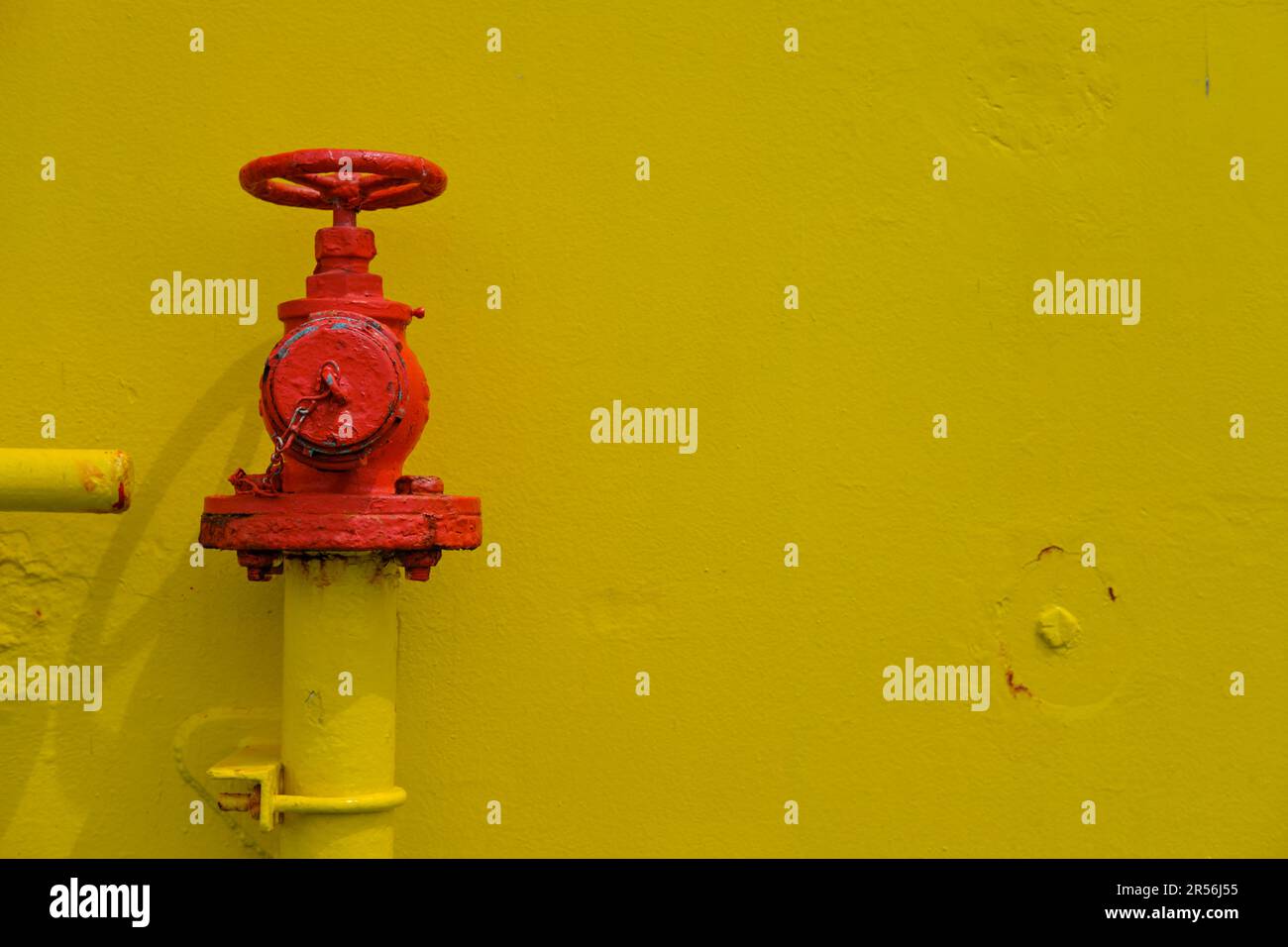 A red painted fire hydrant valve with a wheel for shutting and opening the flow of water. Firefighting hydrant valve painted red on a yellow wall. Stock Photo