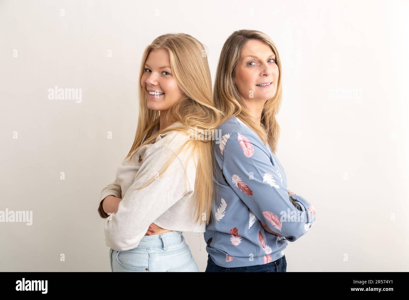 A mother & her adult daughter standing back to back with arms crossed Stock Photo