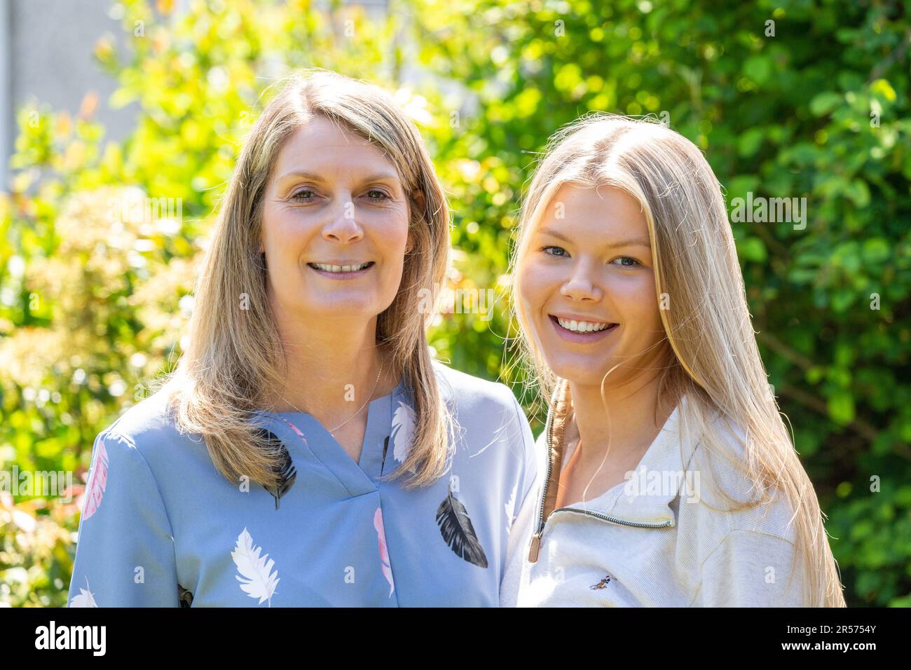 A mother and her adult daughter standing side by side outside in a garden. Stock Photo