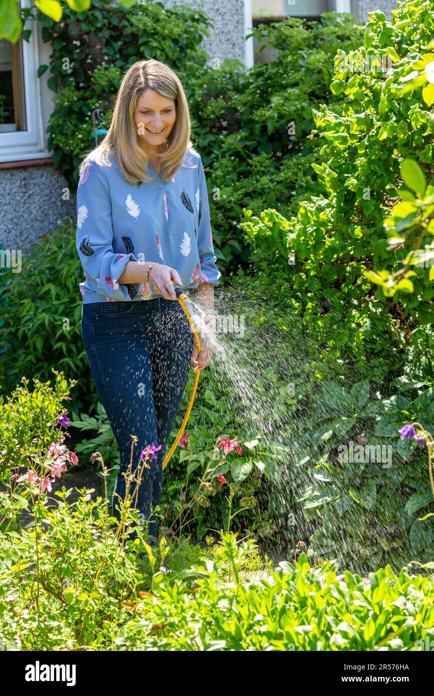 Woman watering garden with hose Stock Photo