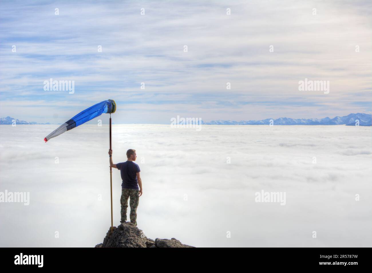 A man with a tall weather vane looks from above at the snowless clouds covering a mountain valley in Bariloche, Argentina Stock Photo