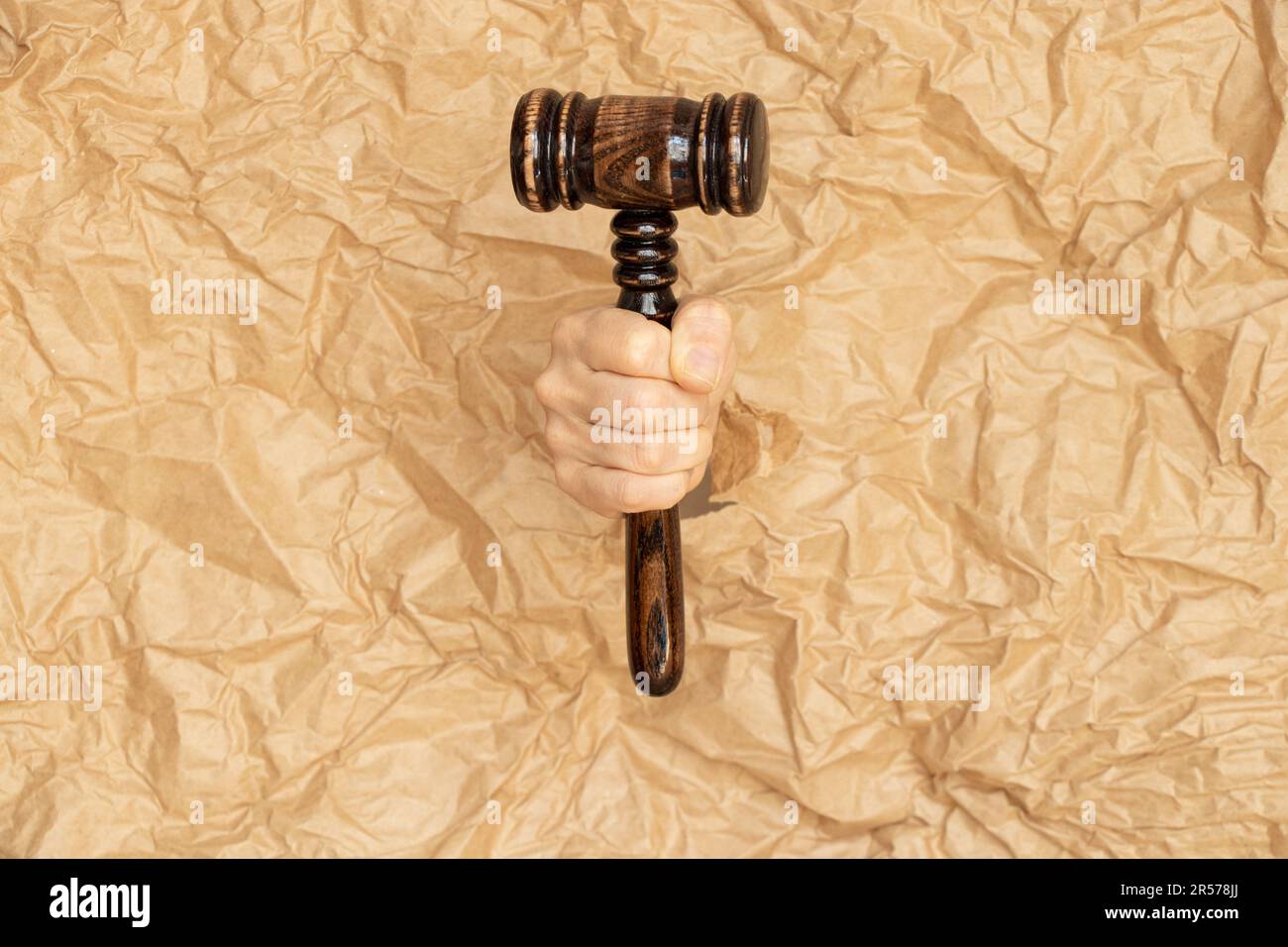 Judge's gavel in girl's hand sticks out of torn brown crumpled paper, court Stock Photo
